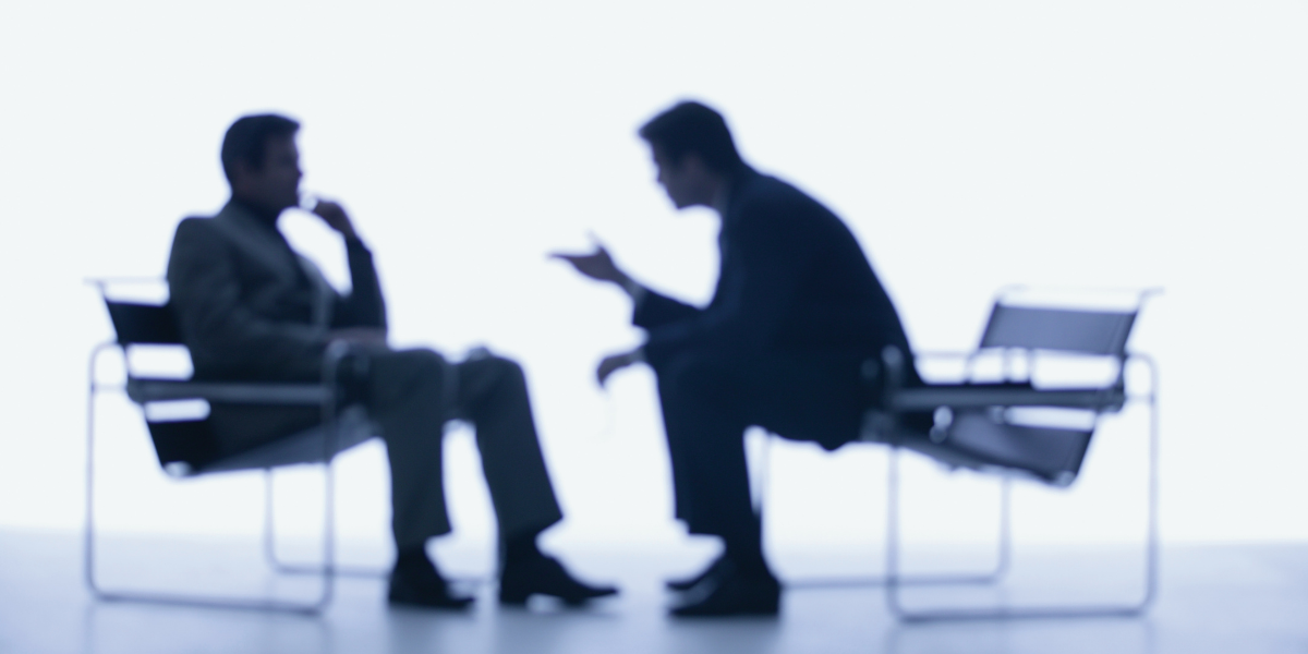 A blurry image of two men sitting across from eachother appearing to be conversing with eachother.